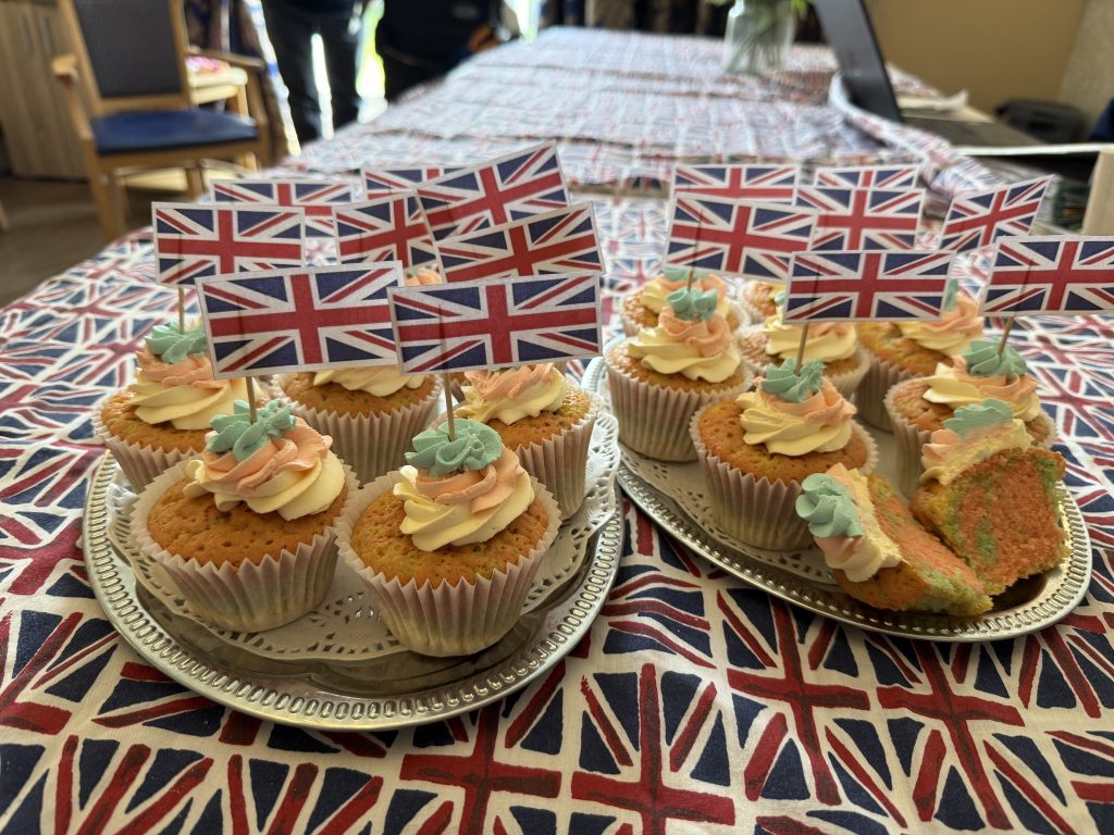 Plates of decorated cupcakes with Union Jack flags displayed on a patterned tablecloth.