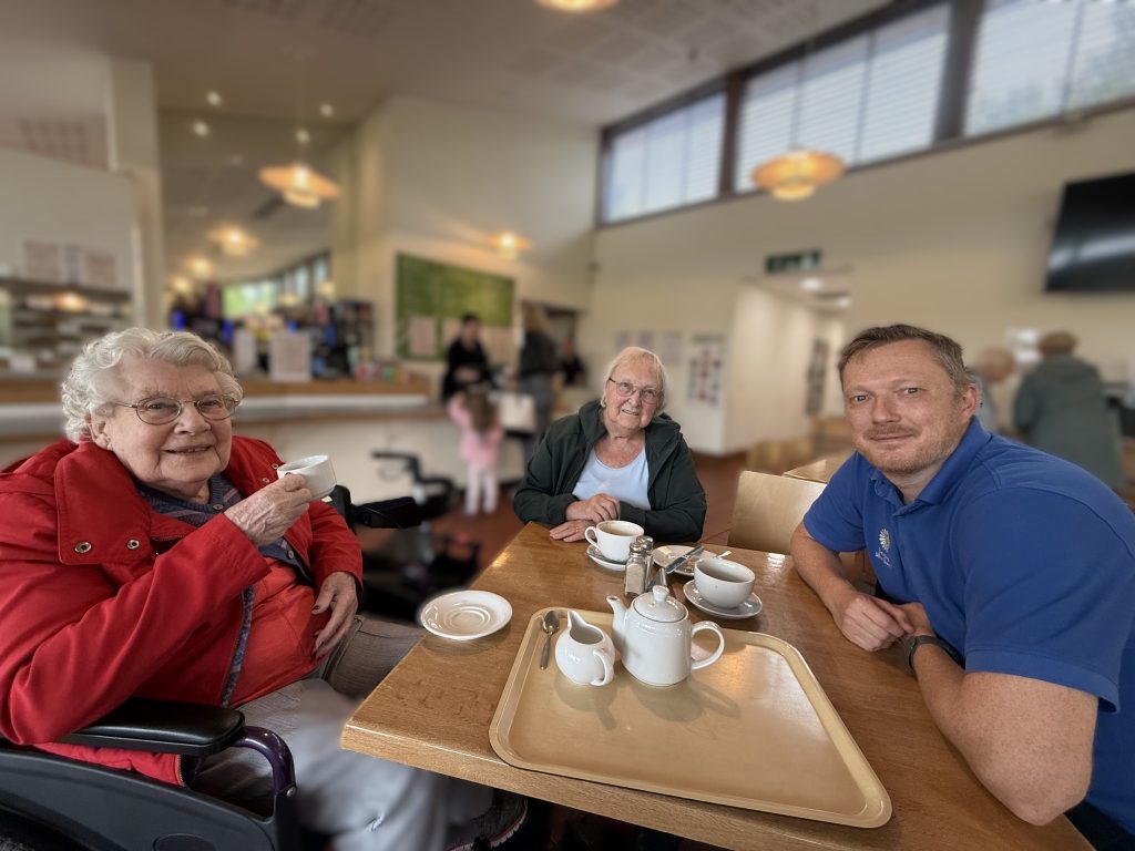 Two elderly women and a caregiver enjoying tea together at a café.