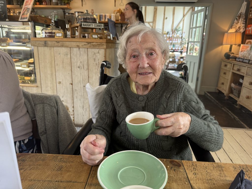 Elderly woman in a wheelchair smiles while holding a cup of tea in a cozy café.