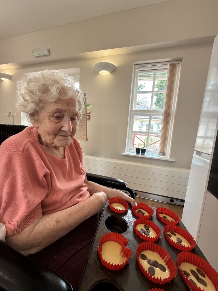 Elderly woman holding a tray of unbaked cupcakes with chocolate chips.