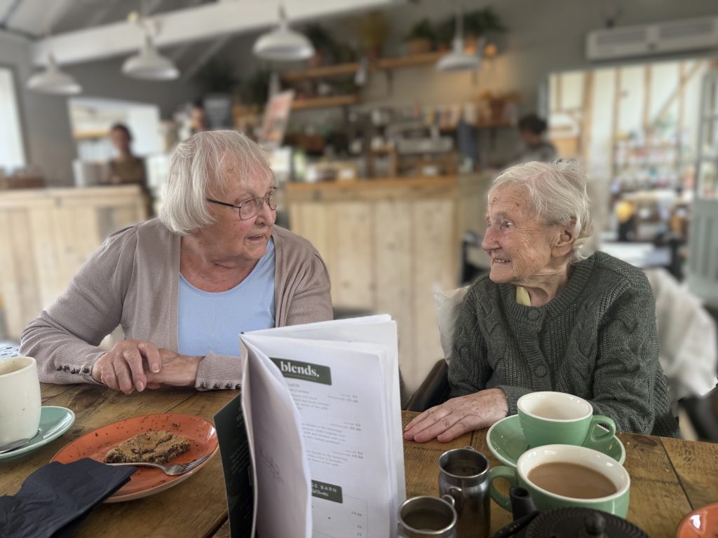 Two elderly women chatting over coffee at a cozy café table.