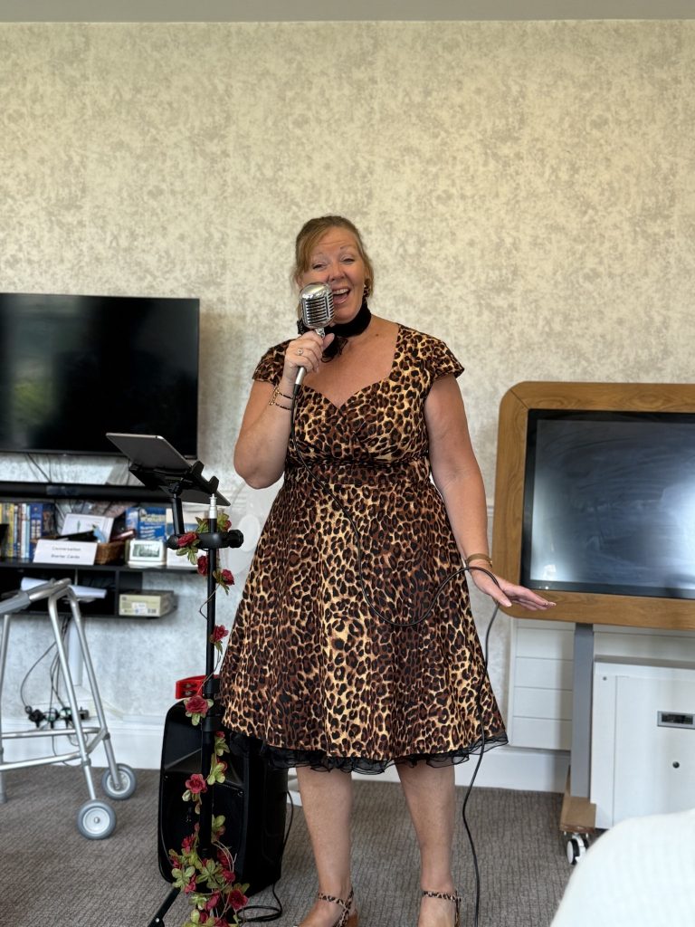 A woman in a leopard-print dress singing into a microphone indoors.