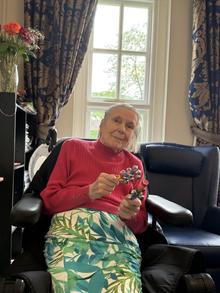 An elderly woman sitting in a chair, smiling and holding small percussion instruments.