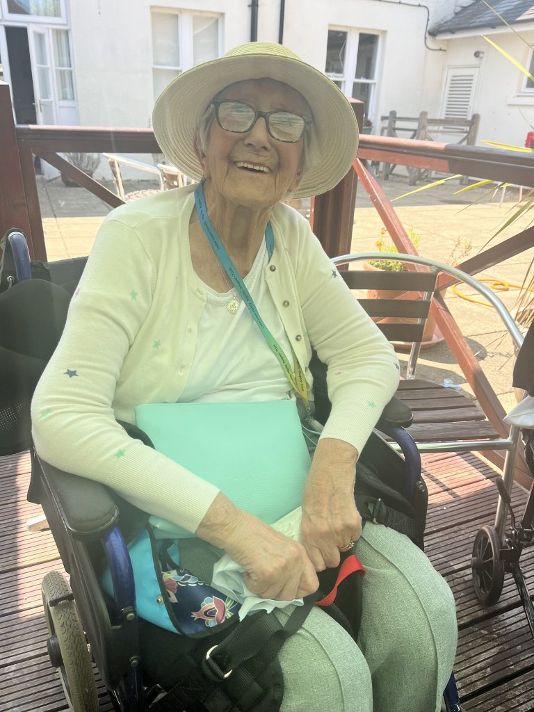 Elderly woman in a wheelchair wearing a sunhat, smiling outdoors.