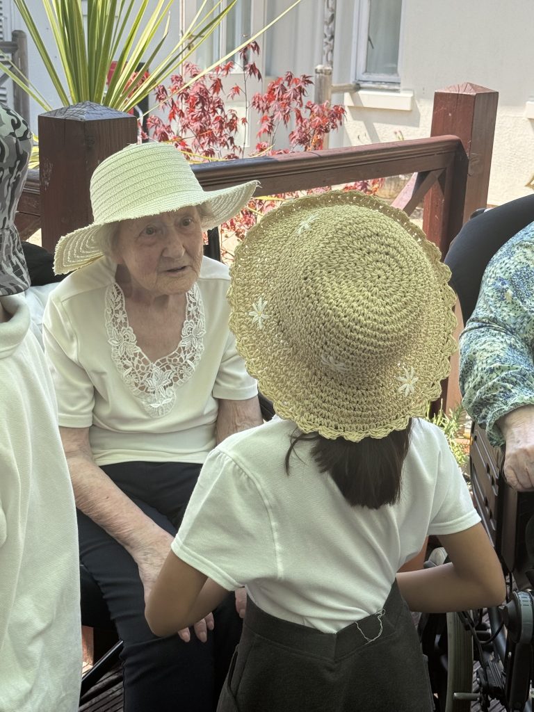 Elderly woman in a sunhat talking with children gathered around her outside.