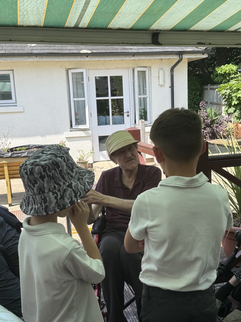 Elderly man in a wheelchair talking with two children on an outdoor patio.