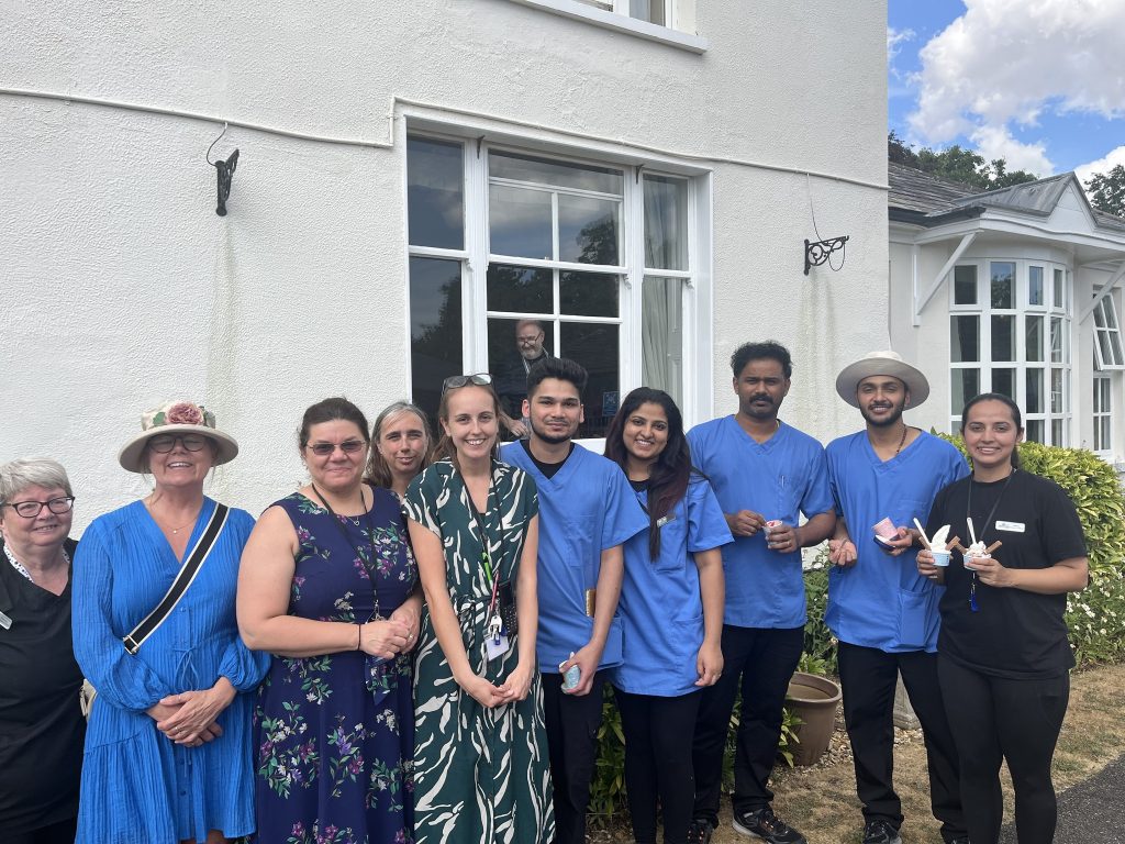 Group of smiling staff and visitors posing together outside a nursing home during a summer event.