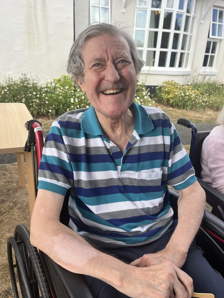 Smiling elderly man sitting in a wheelchair outside a building.