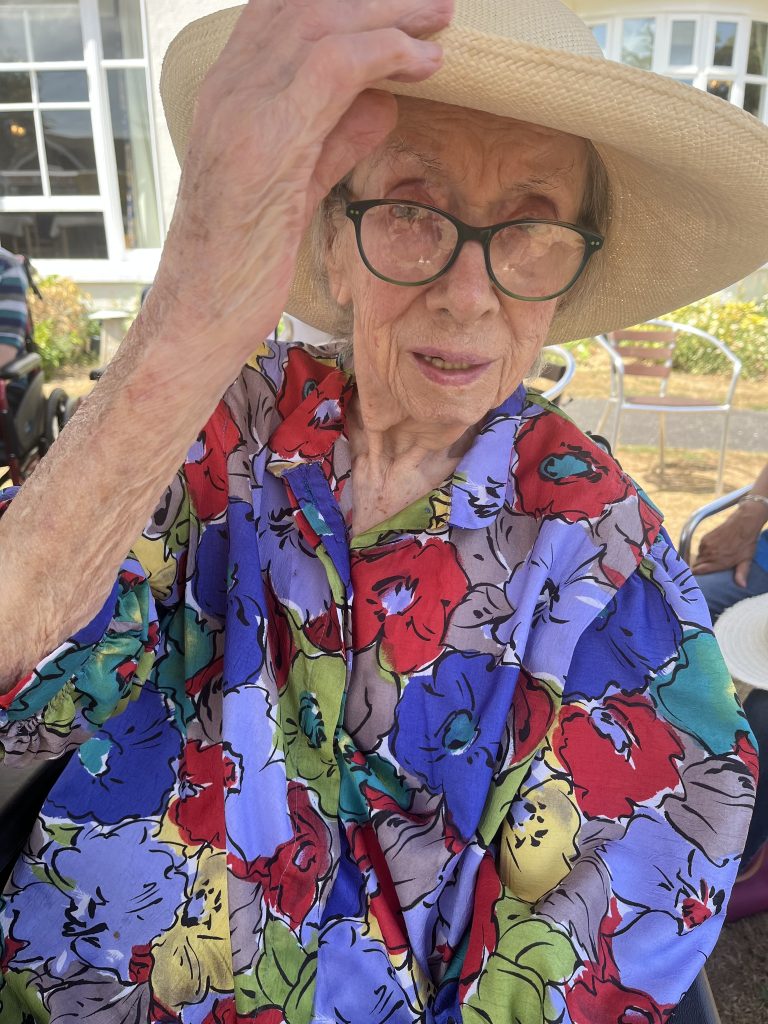 Elderly woman in a colorful shirt adjusting her hat while looking at the camera.