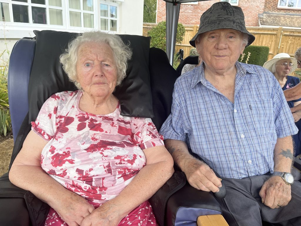 Elderly couple sitting side by side outdoors, looking at the camera.