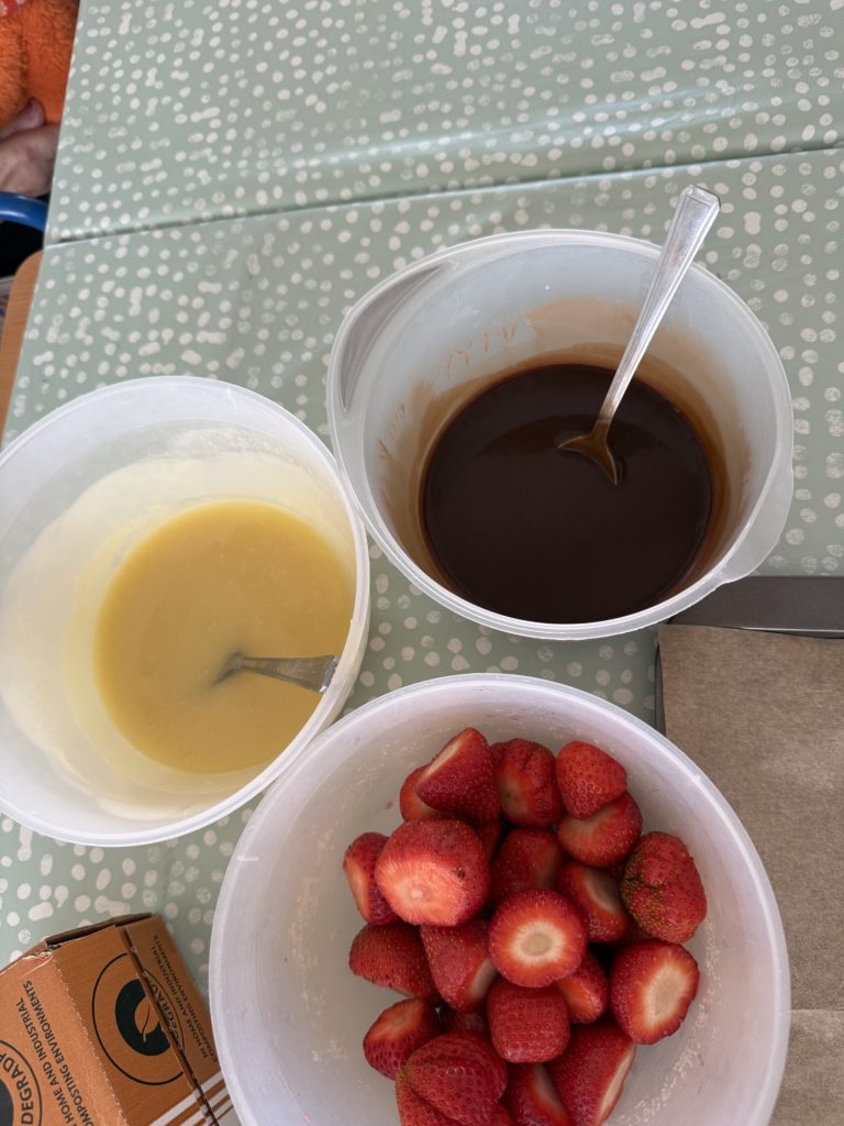 Bowls of melted chocolate and white coating with fresh strawberries ready for dipping.