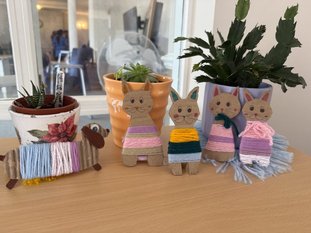 Handmade cardboard animals wrapped in colorful yarn displayed beside potted plants on a table.