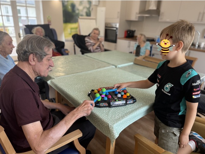 Elderly man and young boy playing a colorful game at a table with others watching.