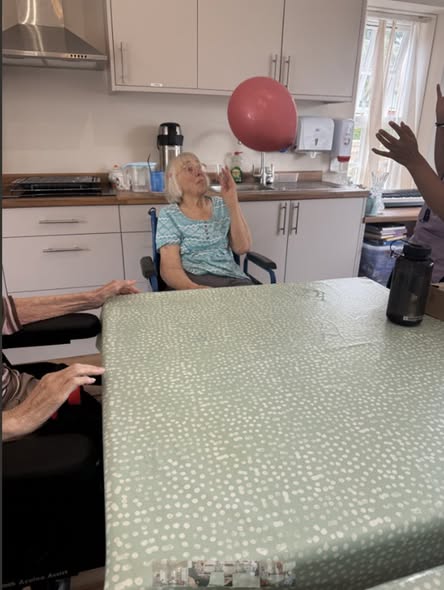 Elderly woman in a wheelchair batting a red balloon during a group activity.