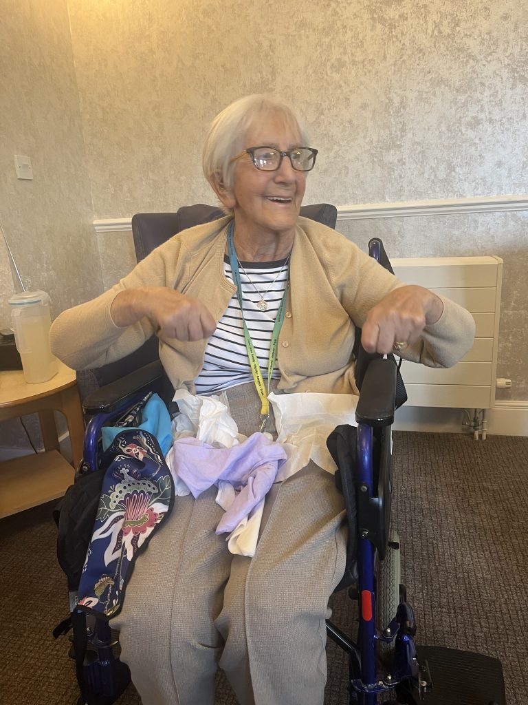 An elderly woman in a wheelchair smiling and moving her arms during an activity session.