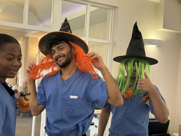 Two staff members in scrubs wearing wigs and witch hats, smiling and posing playfully.