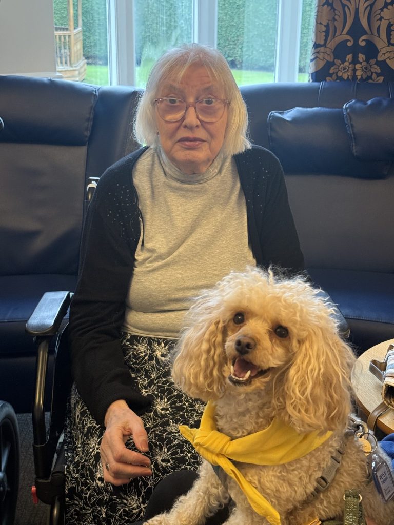 Elderly woman seated with a small dog in a yellow bandana on her lap.