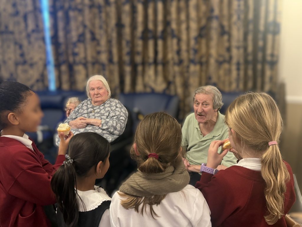 Group of children and elderly residents sharing a conversation and snacks.