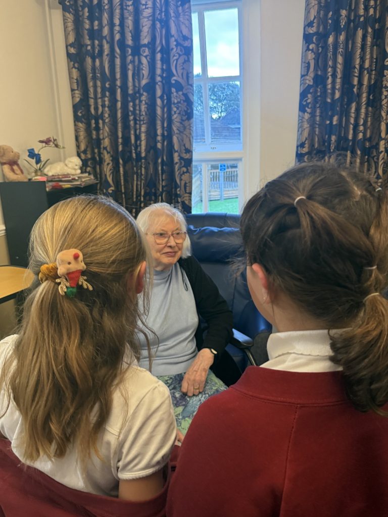 Two children talking with an elderly woman sitting in a chair by a window.