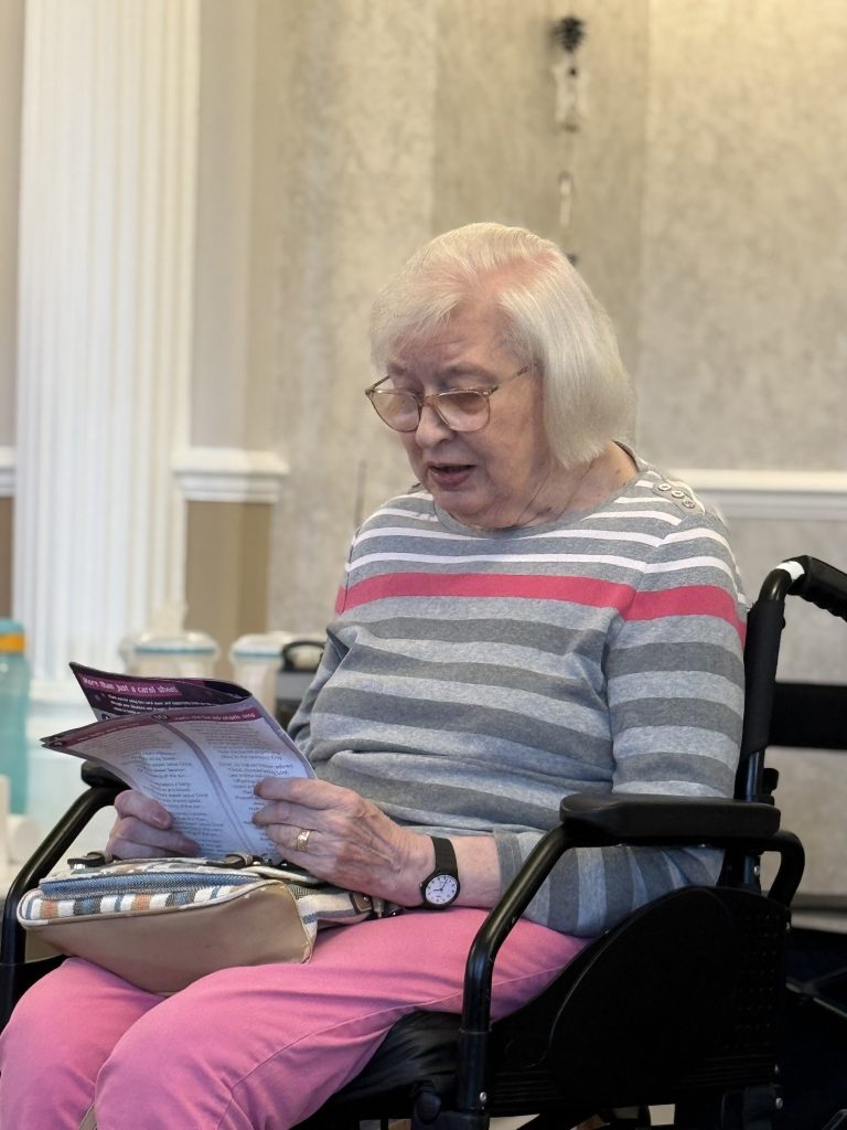 Elderly woman seated in a wheelchair reading a leaflet.