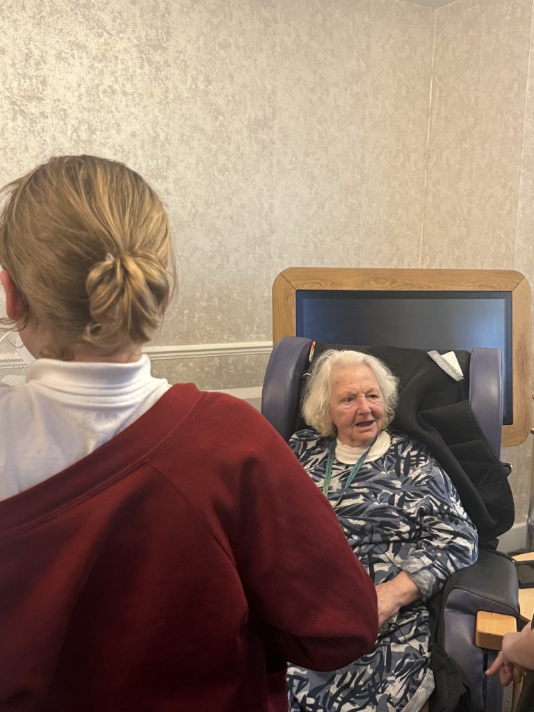 Young visitors speaking with an elderly woman seated in a chair.