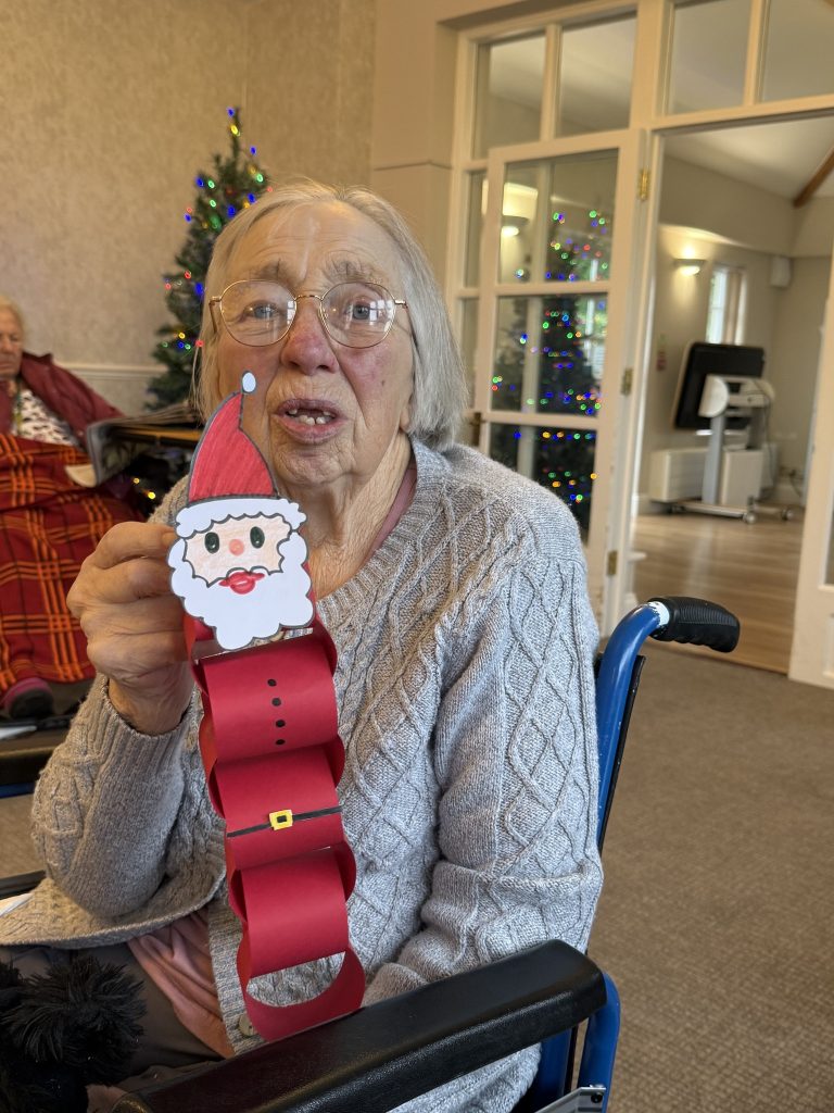 Elderly woman holding a handmade Santa paper chain decoration.