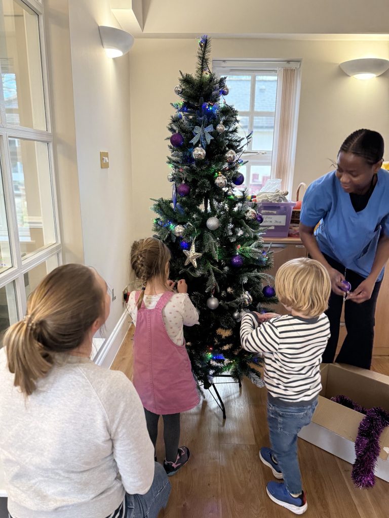 Children and a caregiver decorating a Christmas tree with lights and ornaments.