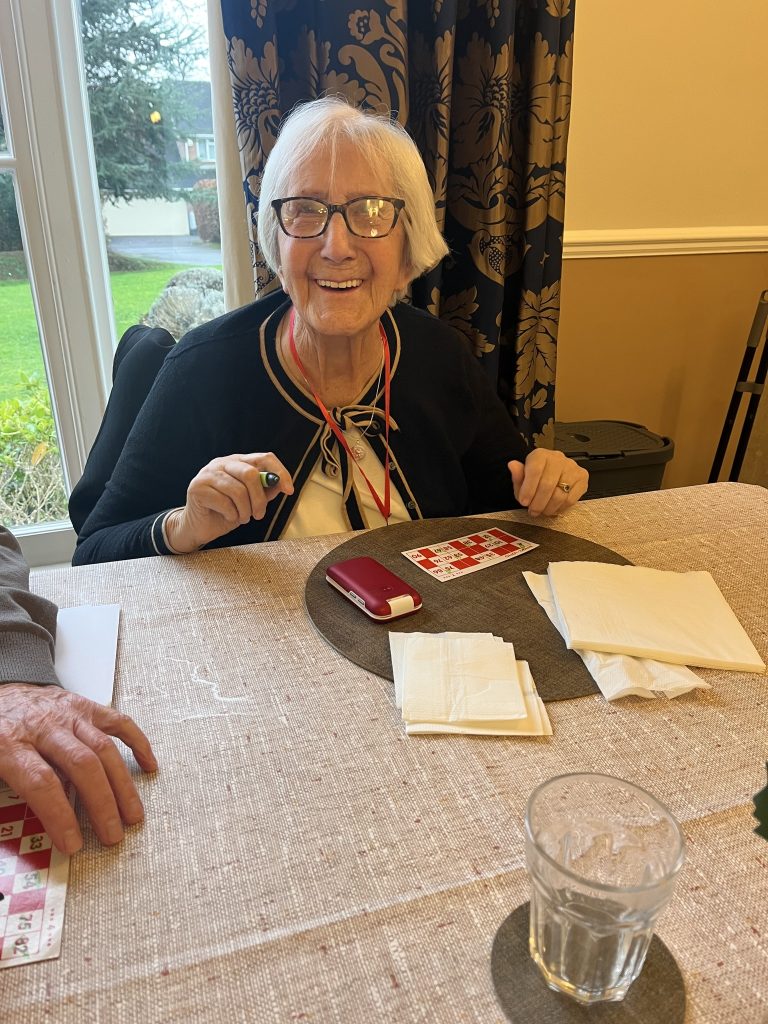 Smiling elderly woman playing a table game with a bingo card in a bright room.