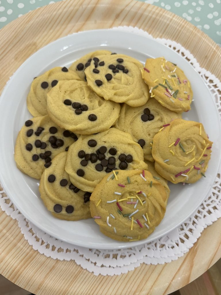 Plate of freshly baked cookies topped with chocolate chips and colorful sprinkles.