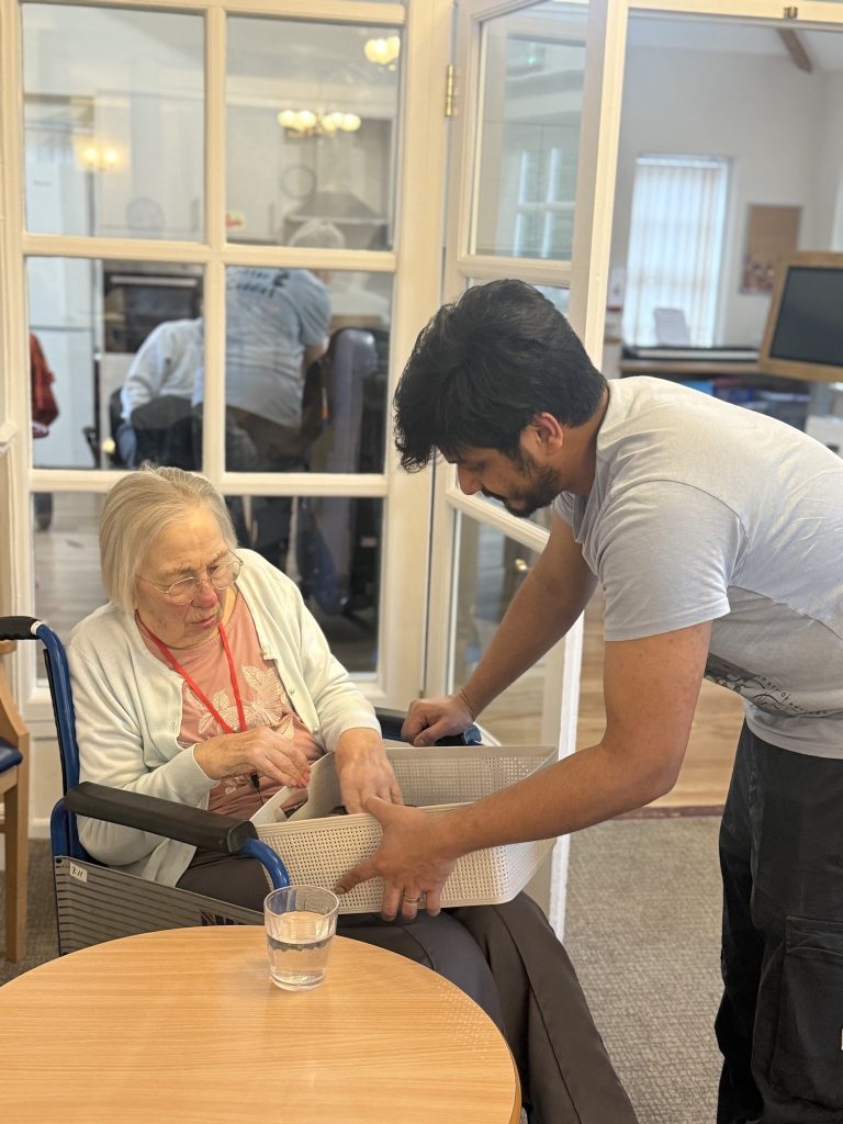 Caregiver helping an elderly woman in a wheelchair interact with an item in a basket.