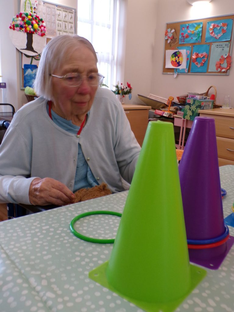 Elderly woman playing a ring toss game with colorful cones on a table.