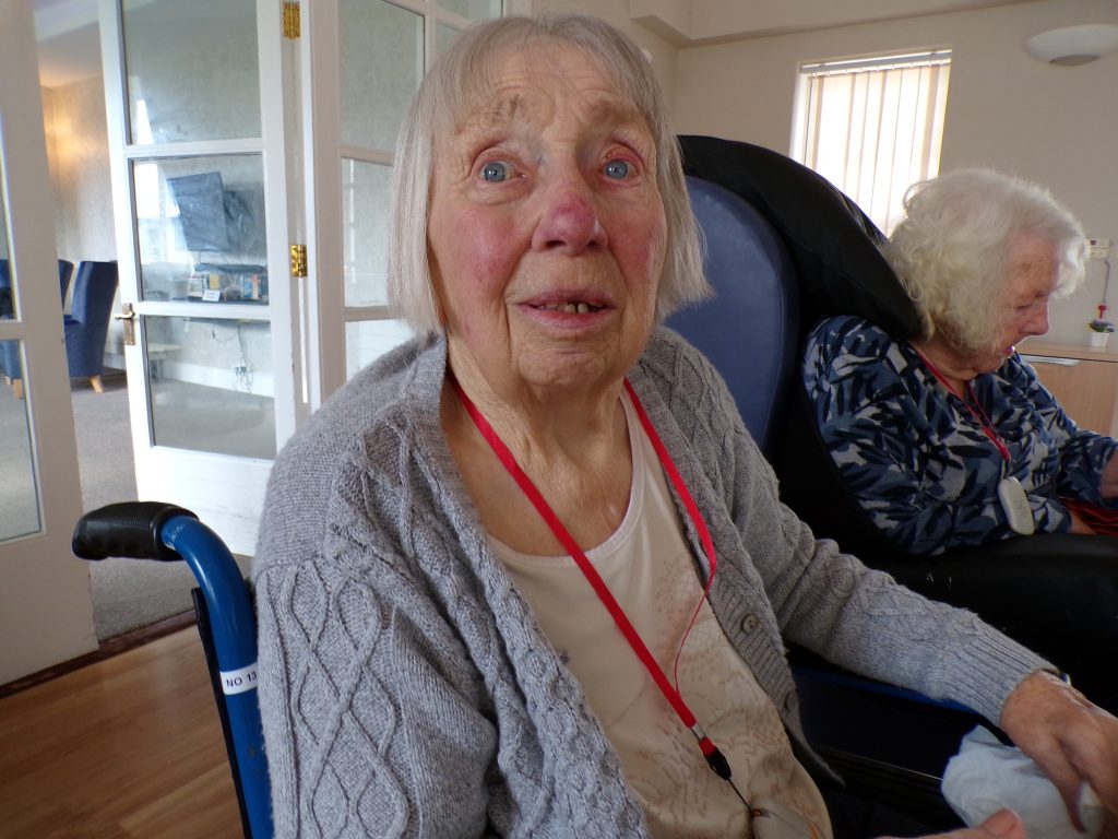 Elderly woman in a wheelchair looking at the camera in a care home.