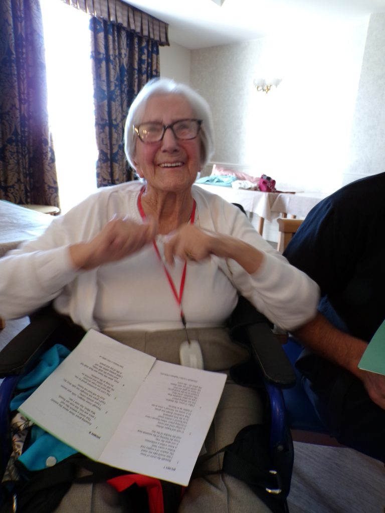 Smiling elderly woman holding an open booklet.