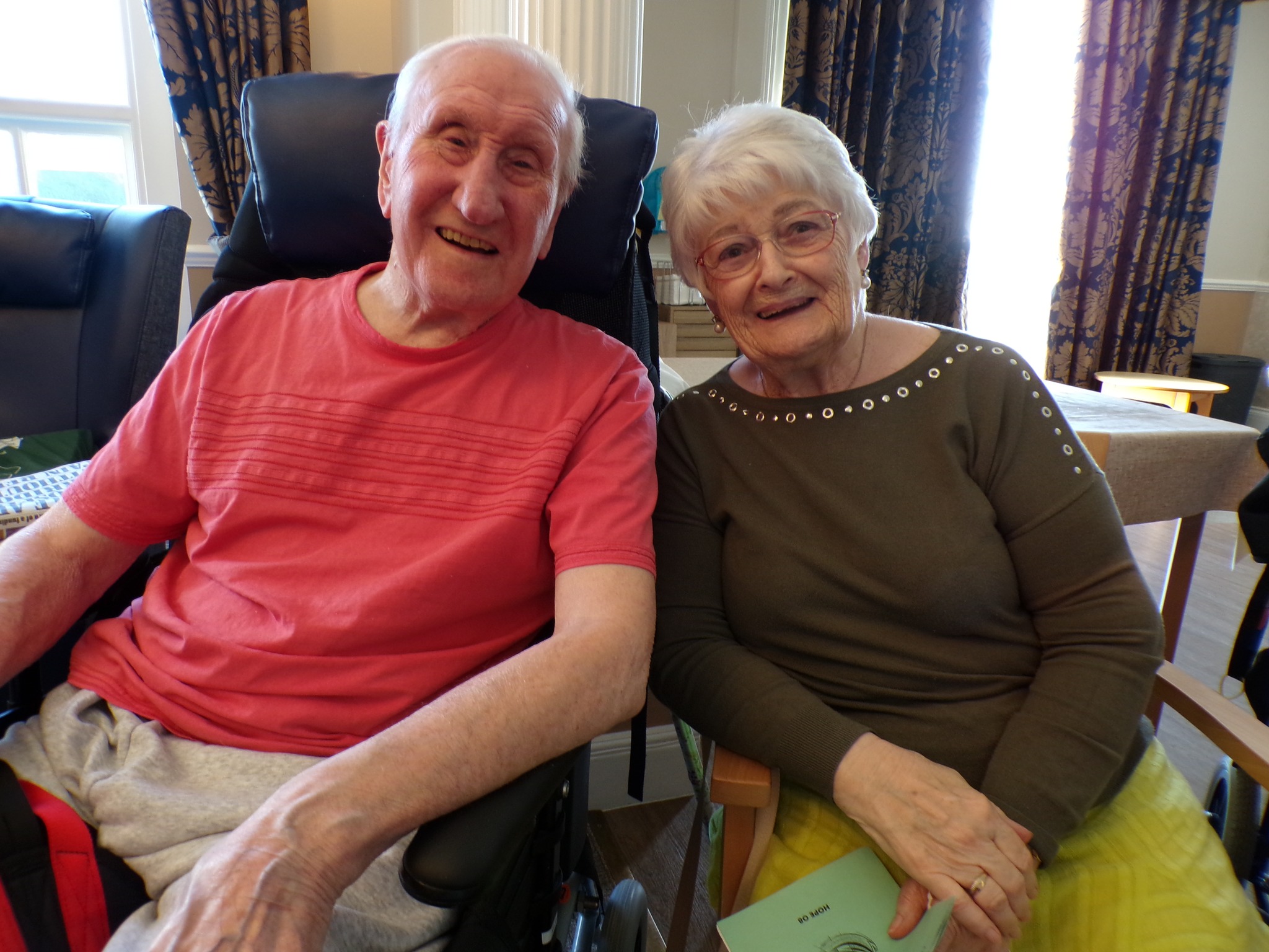 Elderly couple sitting together, smiling at the camera.