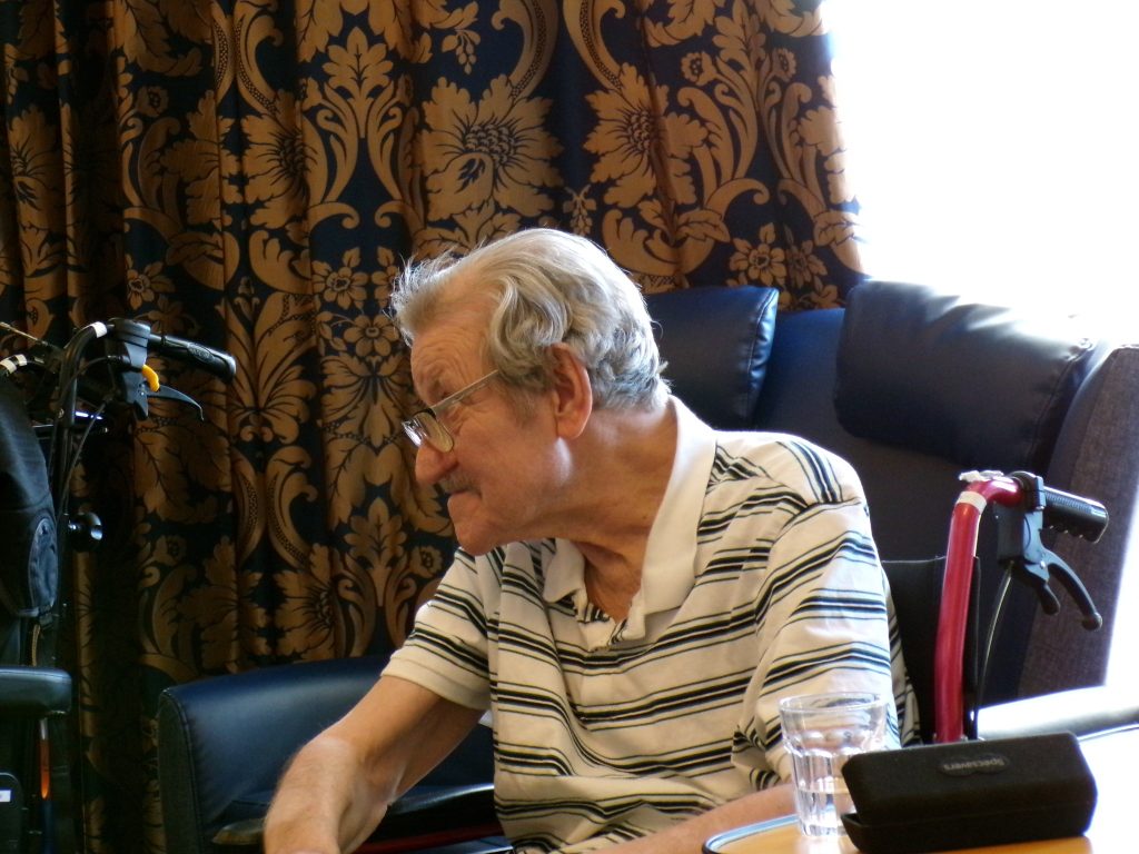 Elderly man sitting in a chair, looking to the side.