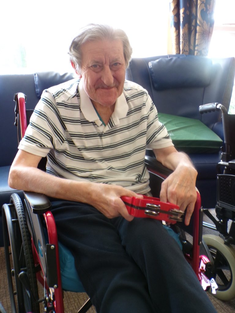 Elderly man in a wheelchair holding a tambourine.
