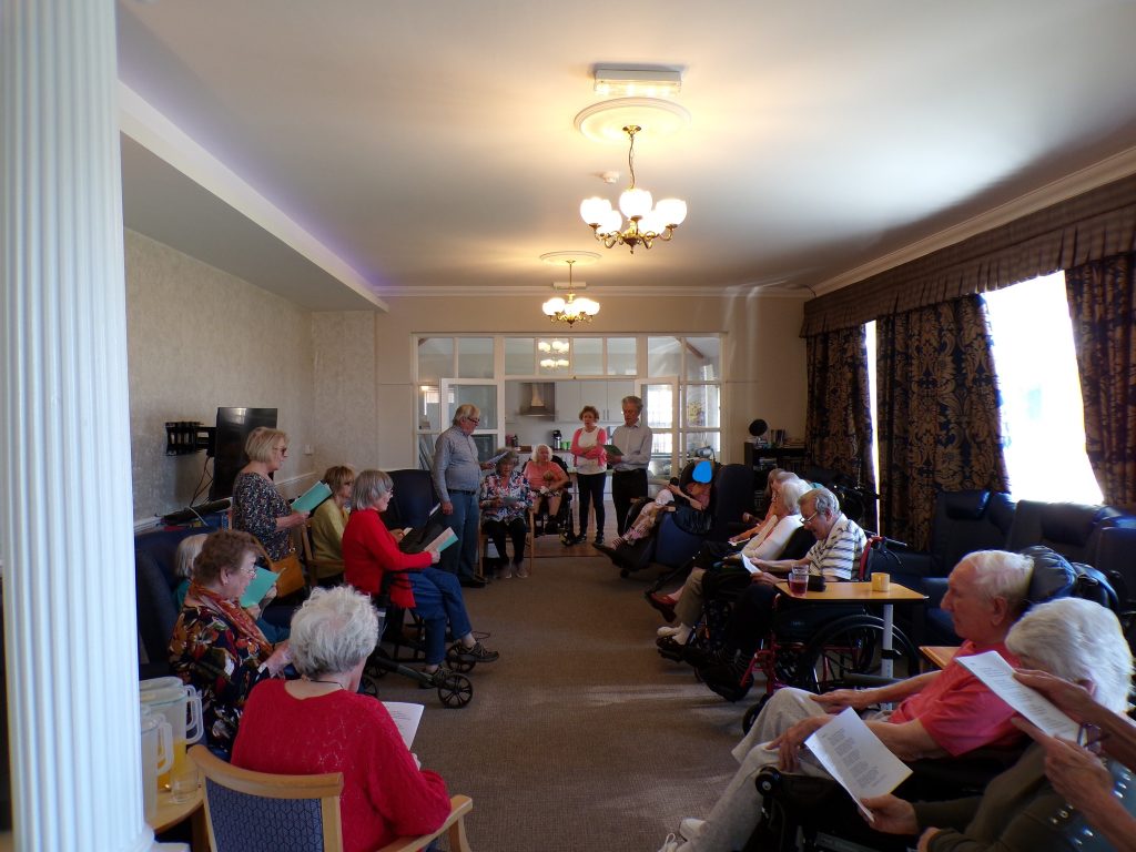 Group of seniors seated in a circle reading or singing together.