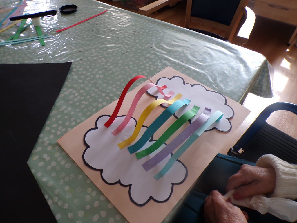Close-up of a paper craft with rainbow-colored strips on a table.