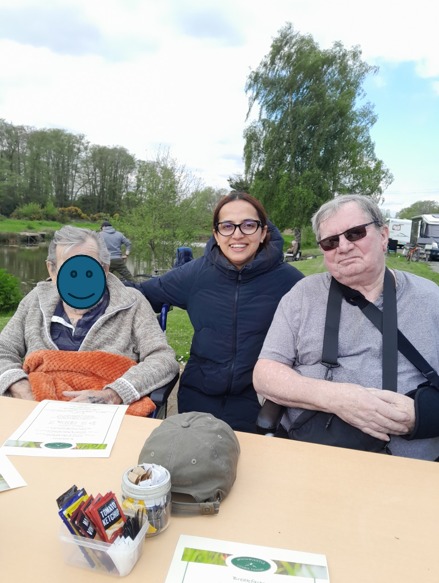 Three people sitting at an outdoor table near a river, smiling at the camera.