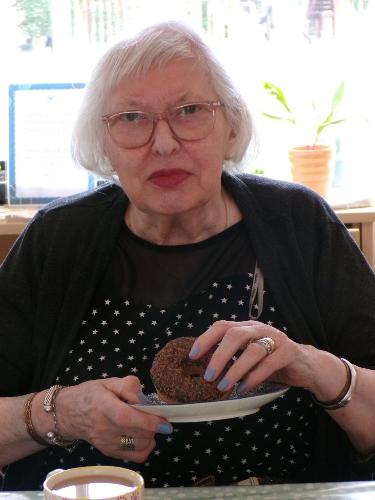 Elderly woman holding a chocolate donut and plate indoors.