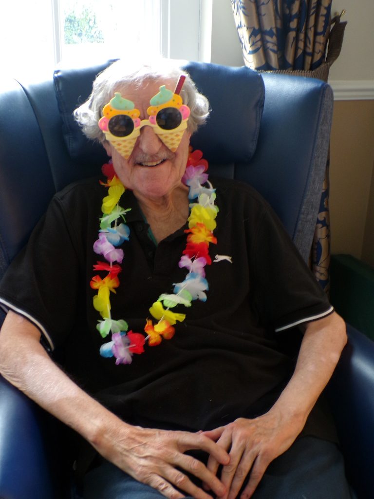 Elderly man wearing colorful party glasses and a flower garland.
