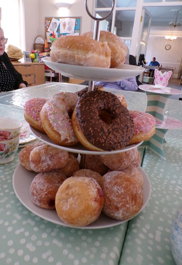 Assorted donuts displayed on a tiered stand at a tea gathering.